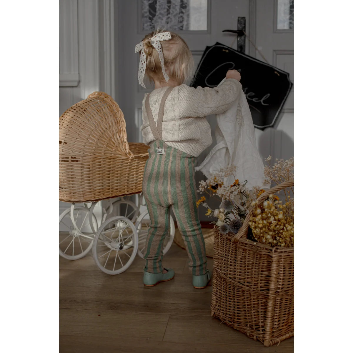 Kind strumpfhose mit trägern und fußlos in matcha und erdnussfarben getragen von kind in gestreifter latzhose