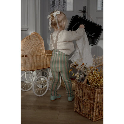 Kind strumpfhose mit trägern und fußlos in matcha und erdnussfarben getragen von kind in gestreifter latzhose