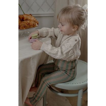 Ein junges kind sitzt am tisch in einer strumpfhose mit träger footless in matcha und peanut farben