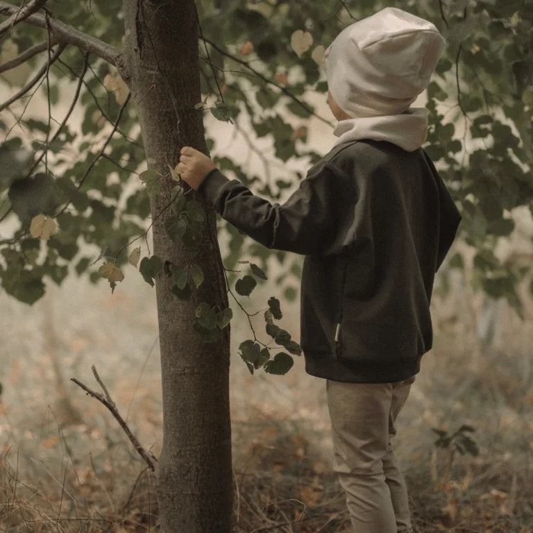 Kinderoutfit mit dunkelgrauem Sweater, hellbraunen Hosen, cremefarbenem Beanie und Schal