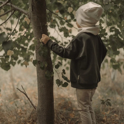 Kinderoutfit mit dunkelgrauem Sweater, hellbraunen Hosen, cremefarbenem Beanie und Schal