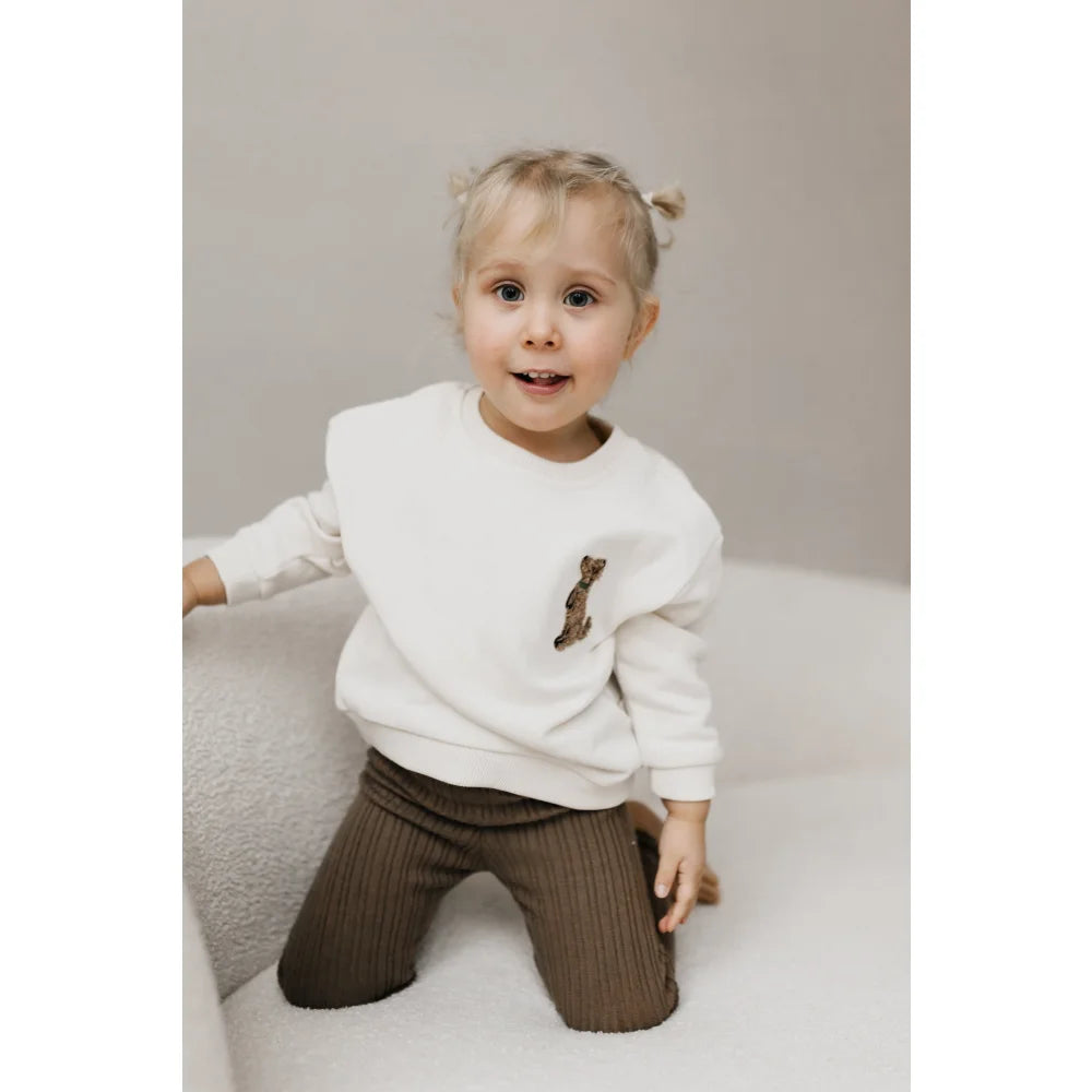 Kind mit weißem Sweater mit Giraffen-Patch und braunen Hosen im Sweater Kids Puppy