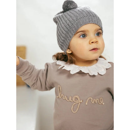 Junger Mensch trägt graue Mütze und taupe Sweatshirt mit Hug Me Stickerei