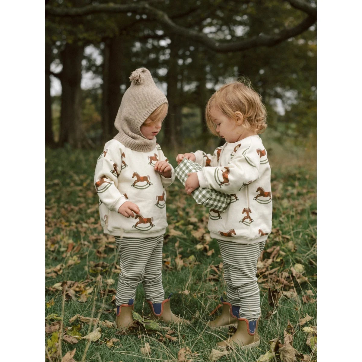Kinder in passenden cremefarbenen Sweatshirts mit braunem Schaukelpferd-Muster