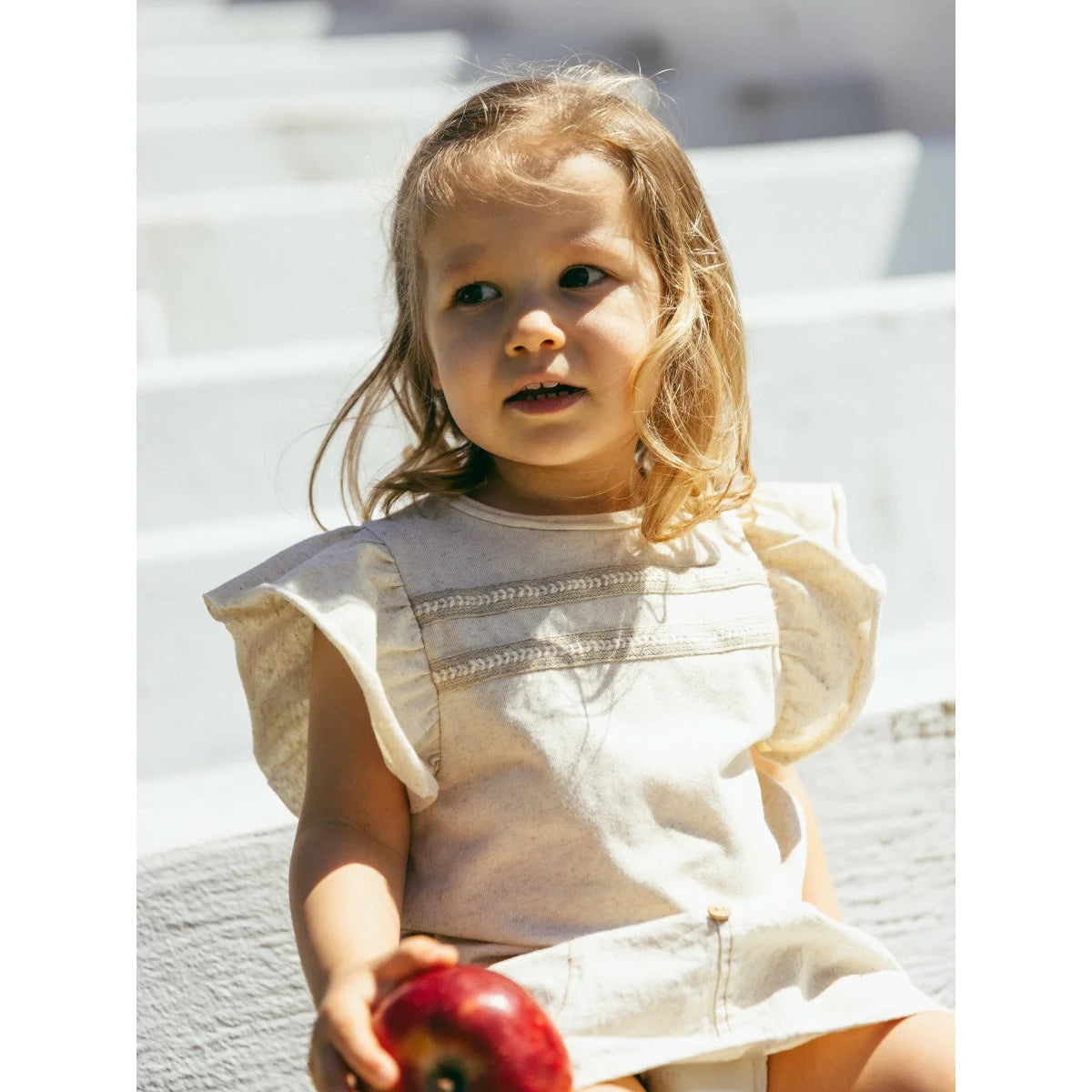 Kind mit englischer Stickerei, elegante Note, hält roten Apfel