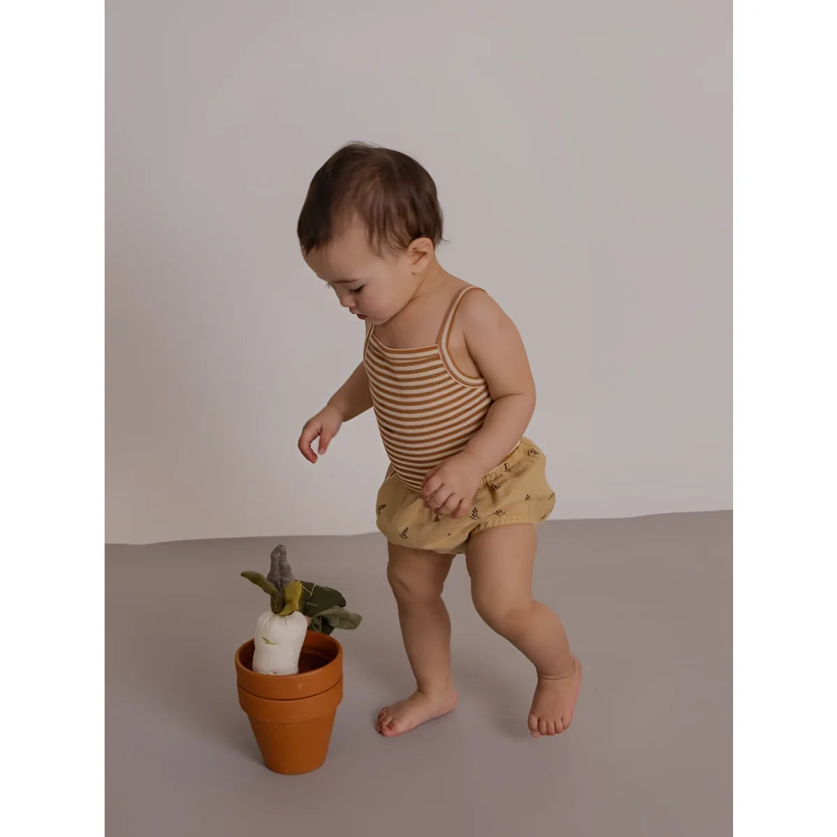 Baby in Tank Bodysuit Copper Stripes neben Terrakottatopf mit Pflanze