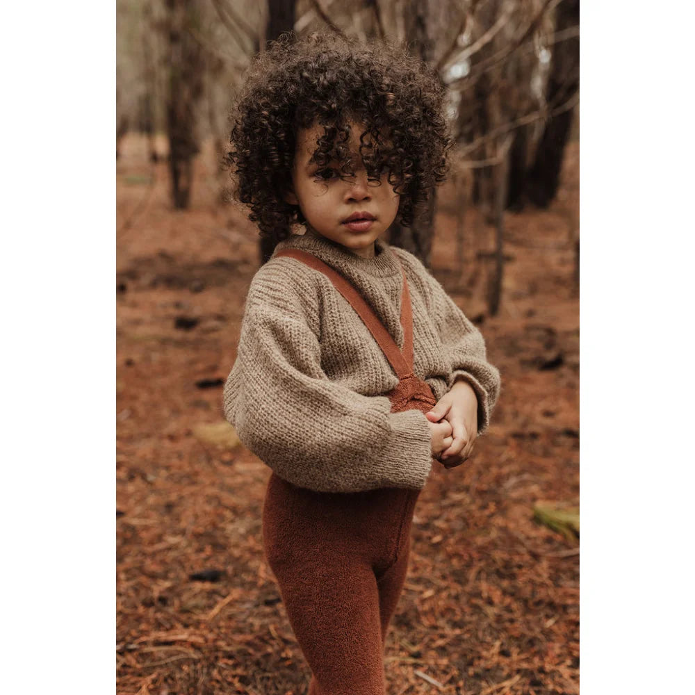 Junger Kind mit lockigem Haar in Herbstwald mit Teddy Warmy Strumpfhosen in Zimt