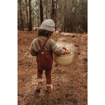 Kind im Overall und Strickmütze trägt einen Korb im Wald für Teddy Warmy Strumpfhose