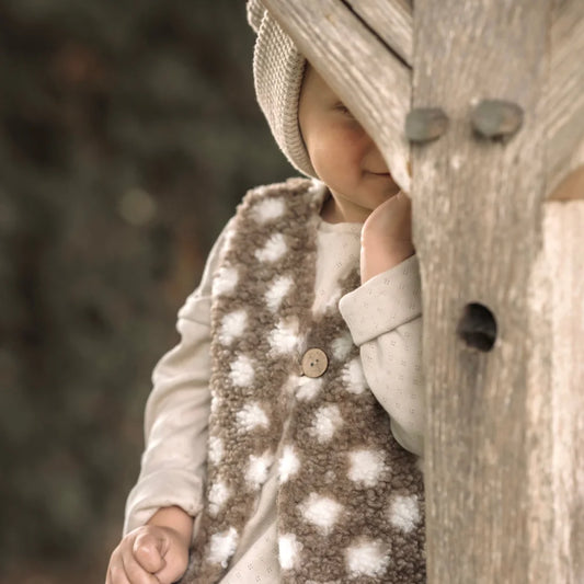 Baby mit gestricktem Hut und gepunkteter Weste hinter Holzstruktur versteckt