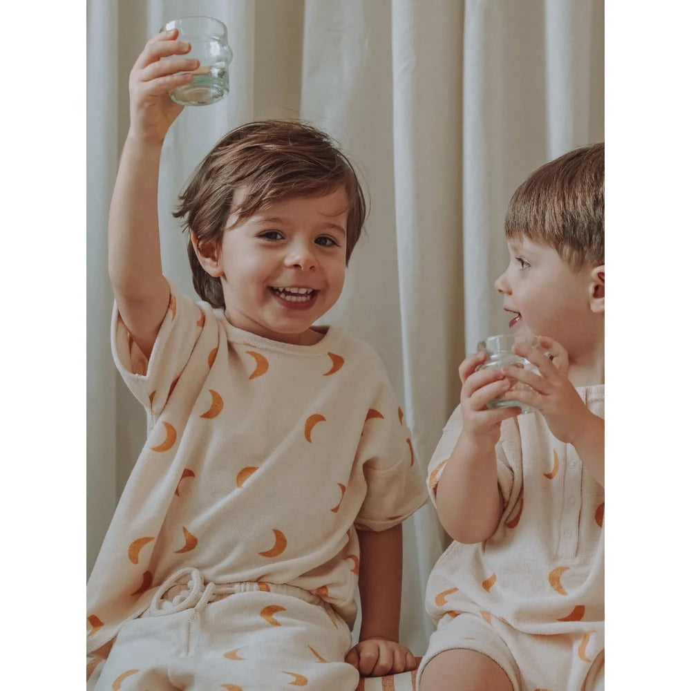 Zwei Kinder in Terry Boxy T-Shirt lächeln, eines hält ein Glas hoch