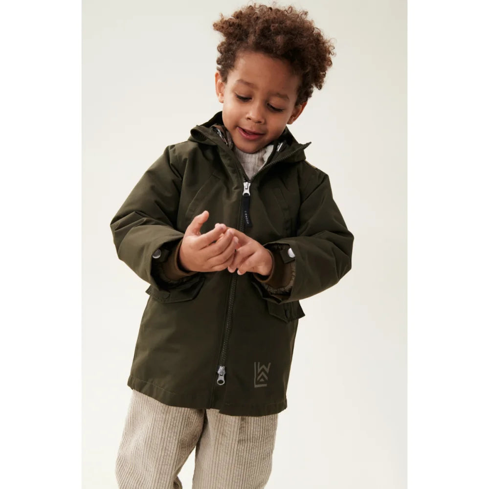 Junge trägt dunkle olivgrüne Timber 2-in-1 Jacke mit Reißverschluss und gestreiften Hosen