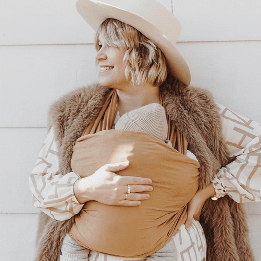 Tragetuch Golden Pecan: Frau trägt Baby in beigefarbenem Stoff
