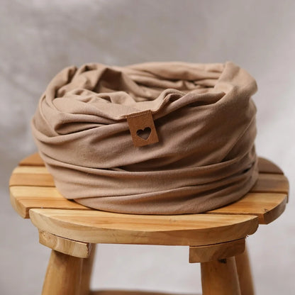 Beige Stoffwickel mit braunem Knopf, gefaltet auf Holzoberfläche. Tragetuch Warm Taupe