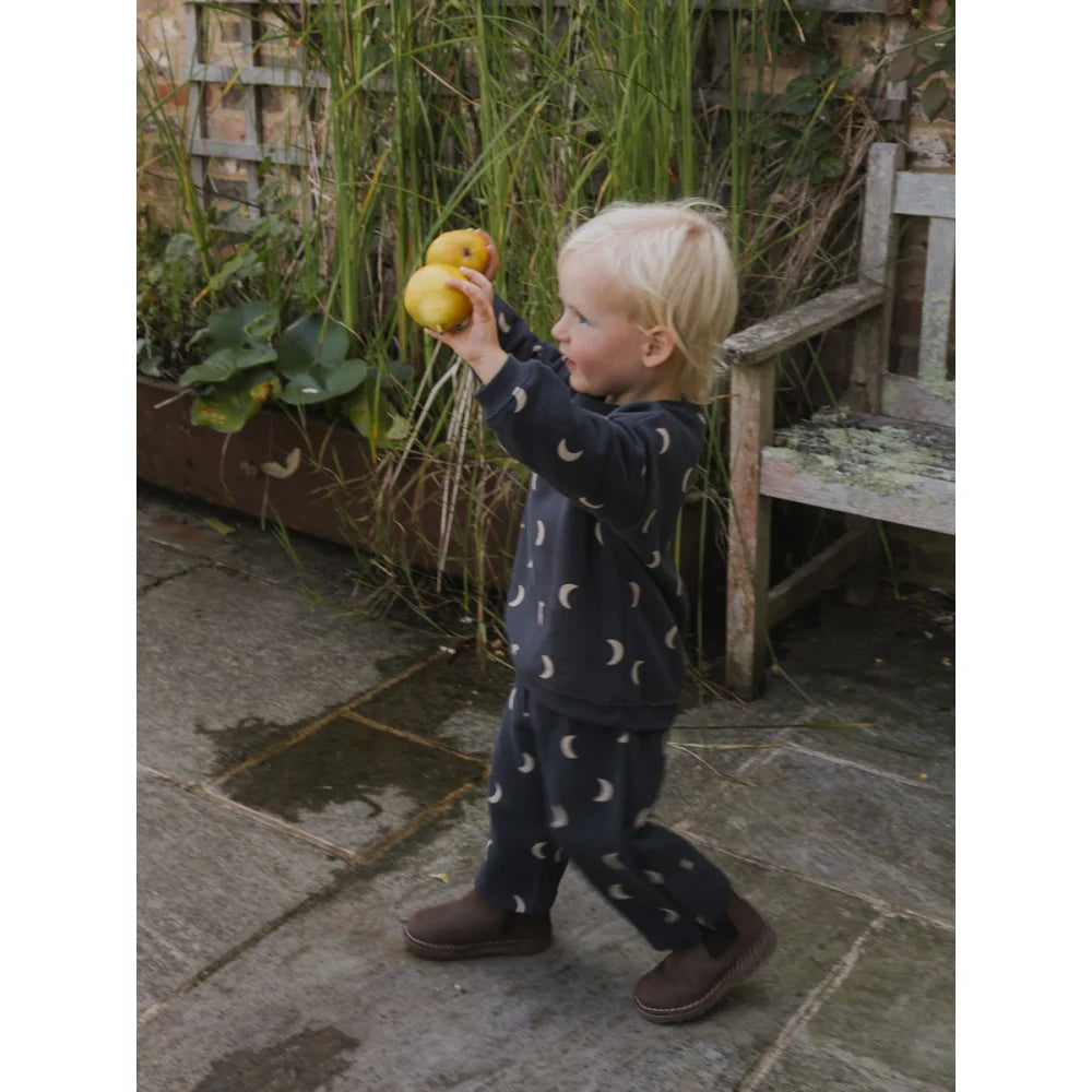 Junges Kind in dunkelblauer Mond-Musterhose hält zwei gelbe Äpfel