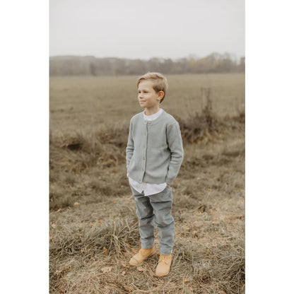 Junge trägt grüne Cordhose mit Ziernähten, weißes Hemd, graue Hose, braune Stiefel