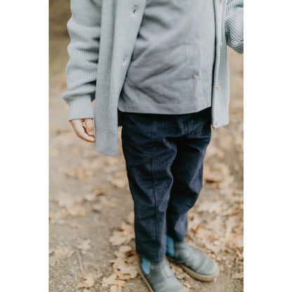 Kinderoutfit mit grauem Cardigan, dunklem Shirt, blauen Hosen und grauen Stiefeln