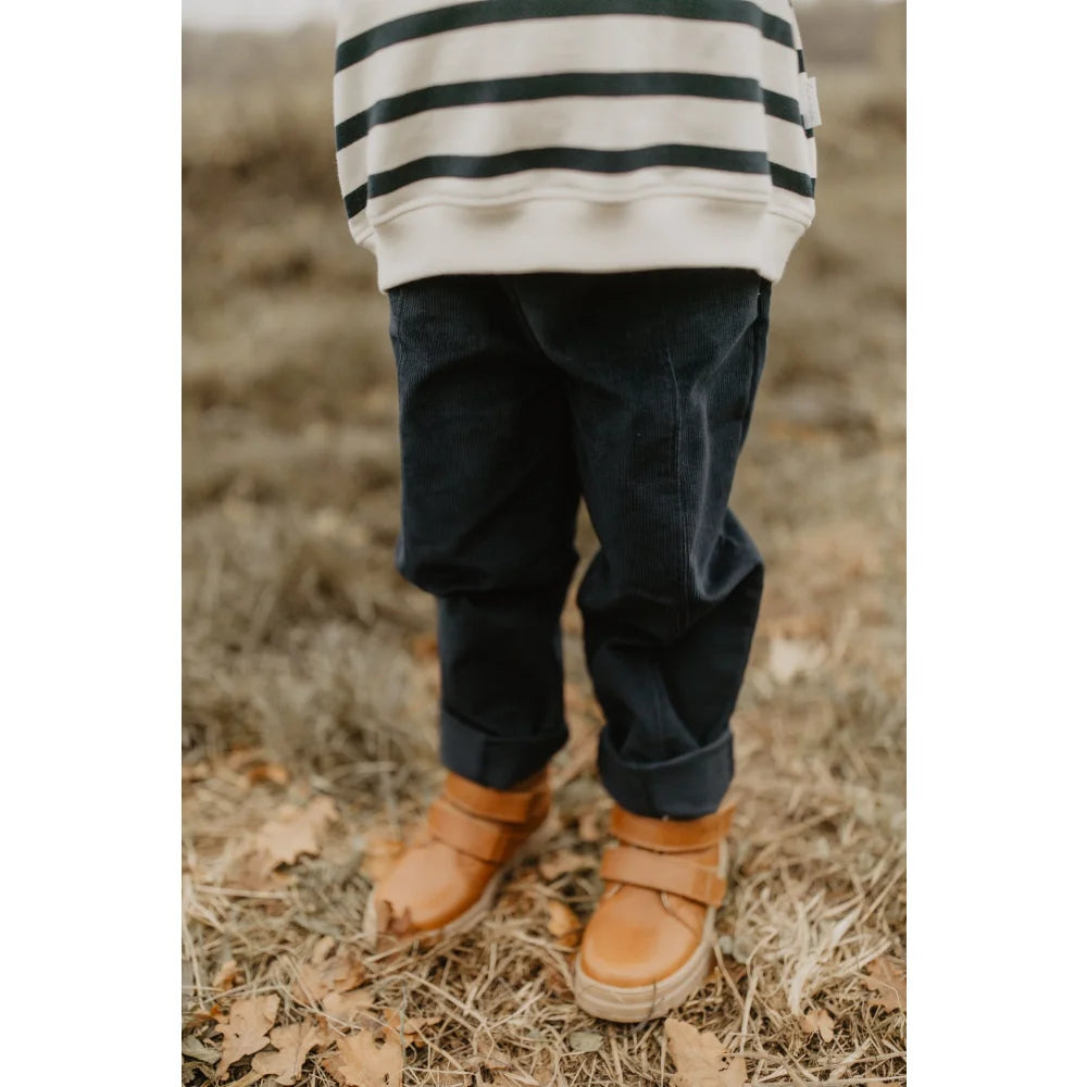 Junge trägt weiße und dunkle gestreifte Cordhose, dunkle Hose und braune Stiefel