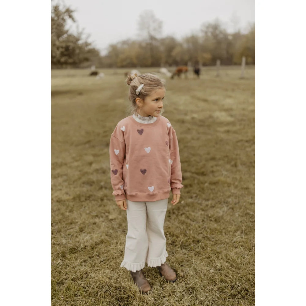 Junge Mädchen in dusty rose Sweatshirt mit Herz, Rüschenhose und braunen Stiefeln