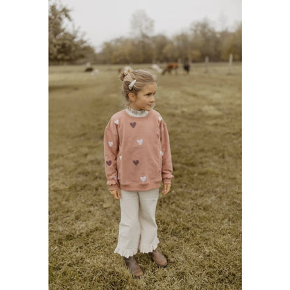 Junge Mädchen in dusty rose Sweatshirt mit Herz, Rüschenhose und braunen Stiefeln