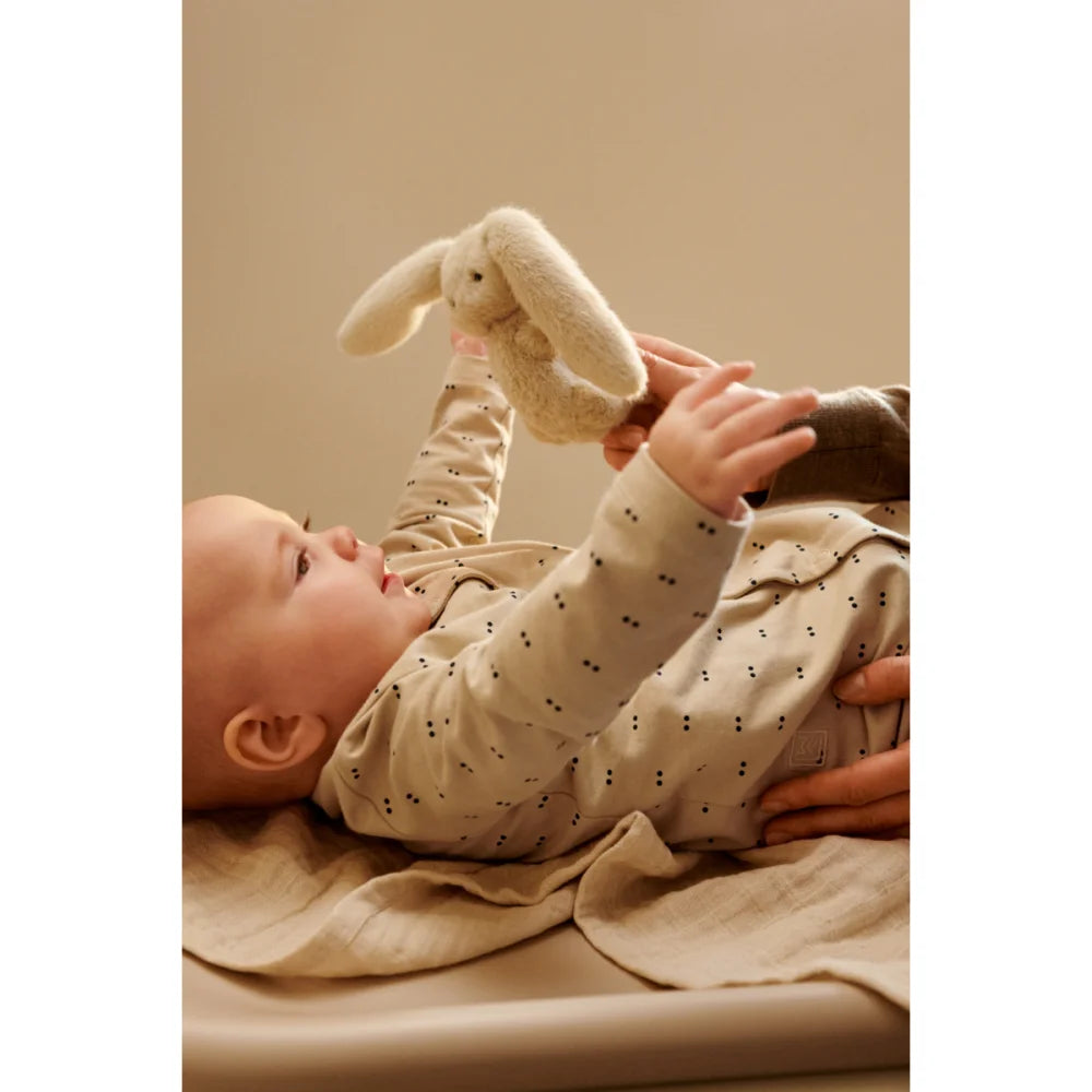 Baby in gepunktetem Langarm-Onsie hält weißen Plüschhasen auf Wickelauflage ohne Bezug Cille Sandy