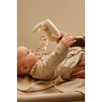 Baby in gepunktetem Langarm-Onsie hält weißen Plüschhasen auf Wickelauflage ohne Bezug Cille Sandy