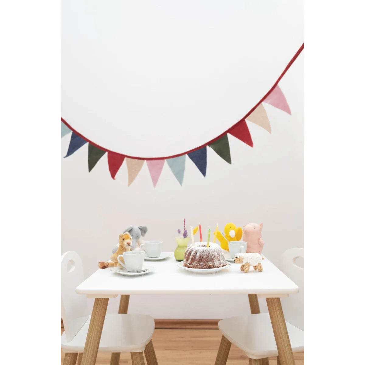 Bunte wimpelkette mit rotem rand aus stoff hängt über einem kindertisch an der wand