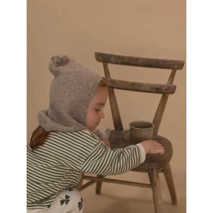 Kindliches Kind trägt eine gestrickte Mütze mit Bommel aus Wolle Oatmeal