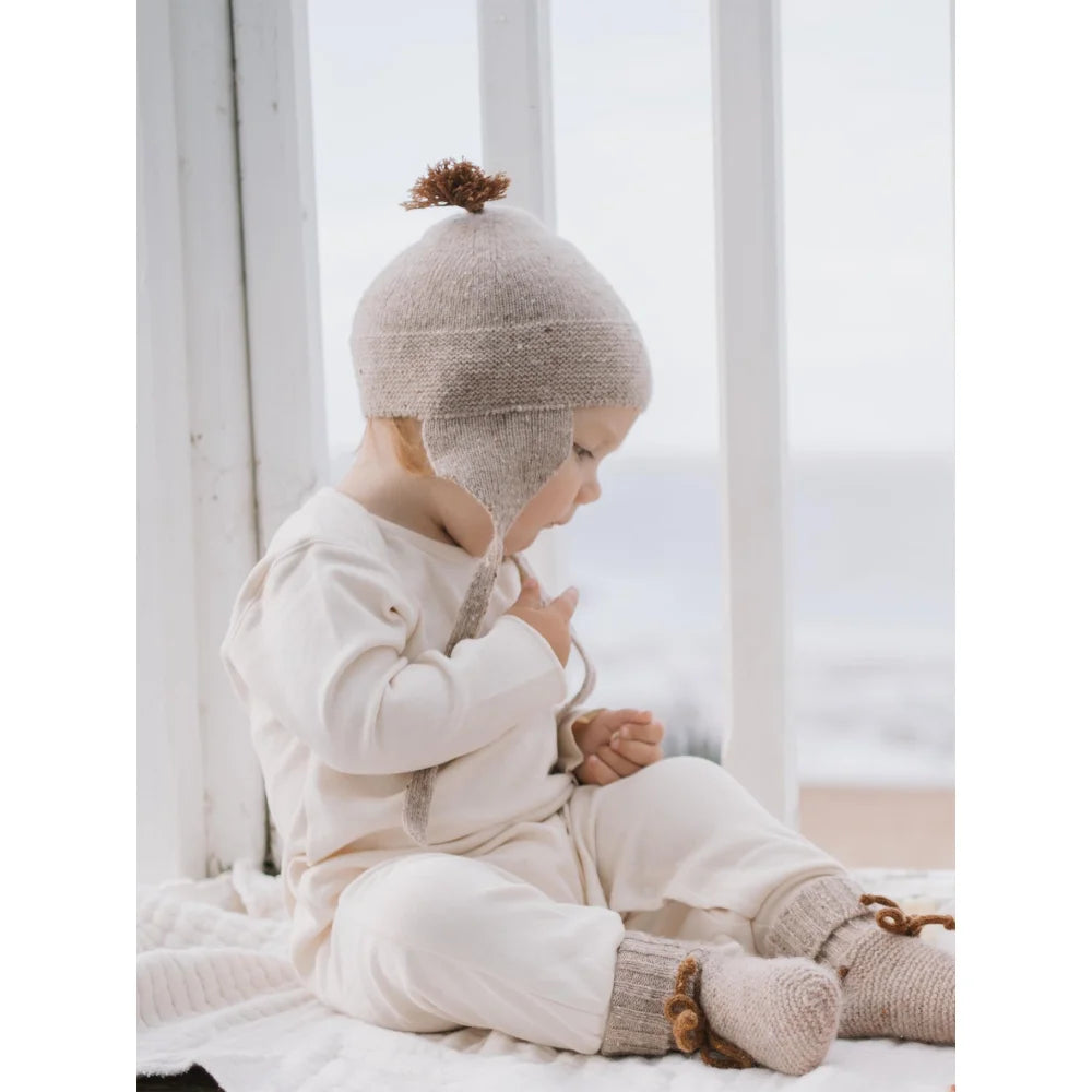 Baby trägt gestrickten Ohrenklappenhut mit Bommel und passenden Booties Wool Booties Oatmeal