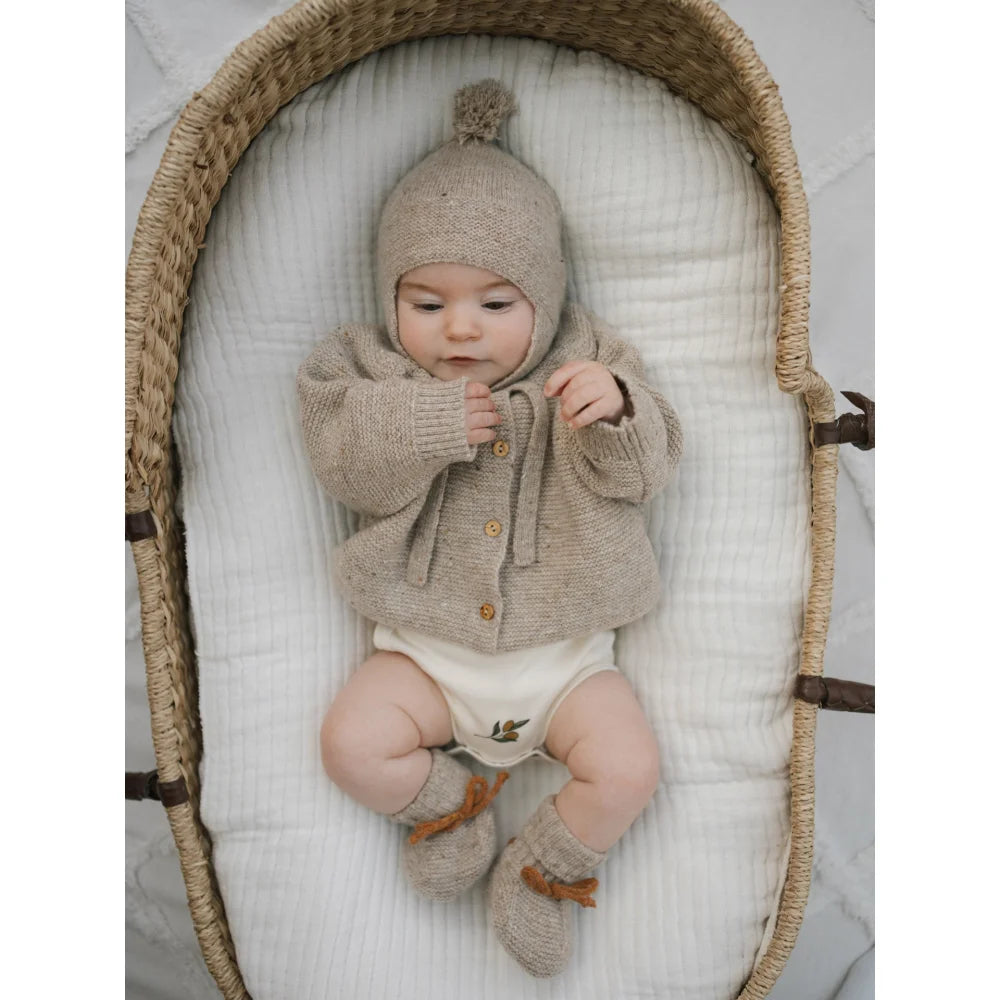 Süßer Säugling in beige gestricktem Wollcardigan, Mütze mit Bommel und Booties