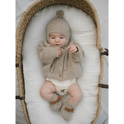 Süßer Säugling in beige gestricktem Wollcardigan, Mütze mit Bommel und Booties