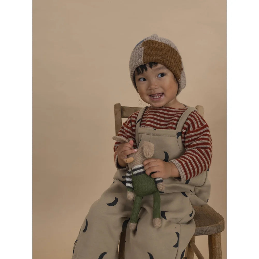 Lächelndes Kind trägt Wool Jumper Paprika Stripes mit Mütze und Kuscheltier