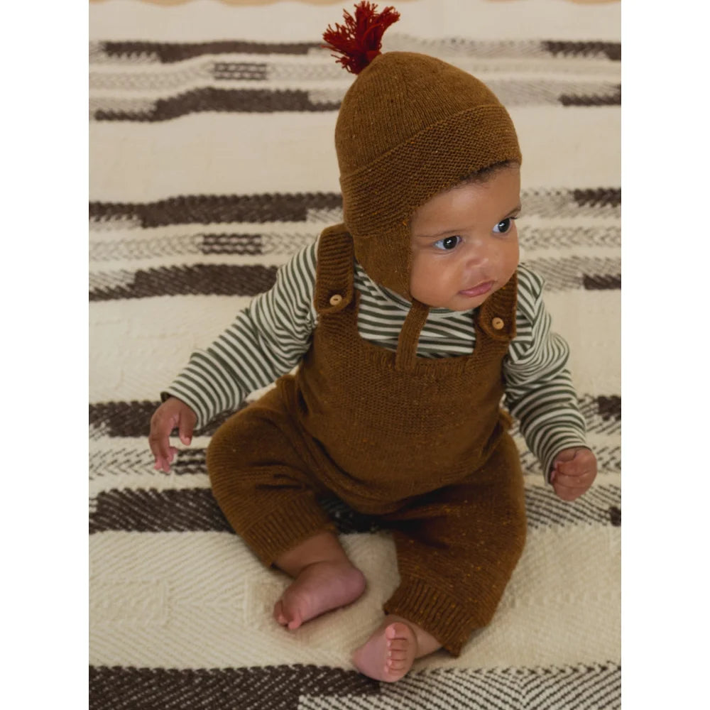 Niedliches Baby trägt braune Strickmütze mit rotem Zopf und passende Overalls