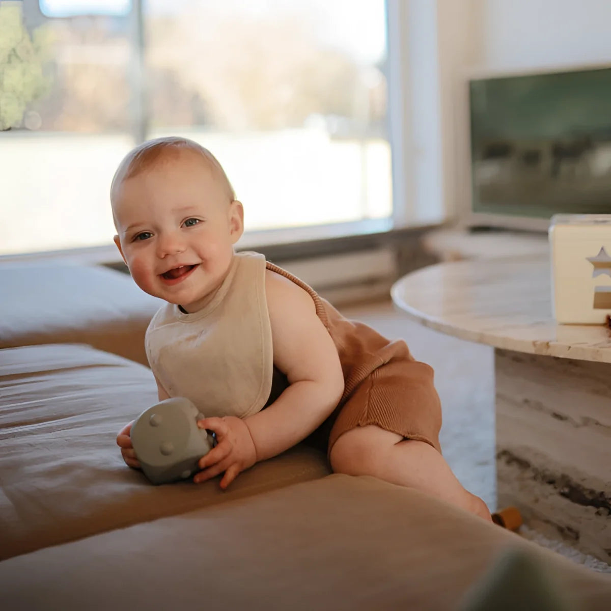 Lächelndes Baby mit Lätzchen beim Würfel Plop-it Spielzeug in Cambridge Blue und Shifting Sand
