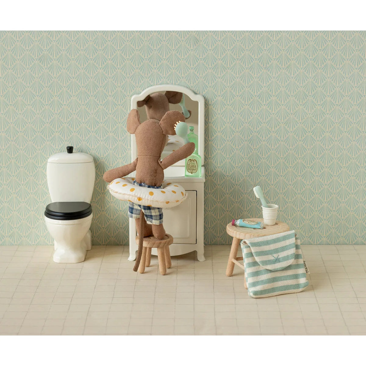 Ein plush brauner mausplüsch in blau gestreiften shorts mit weißem, gelb gepunktetem schwimmring vor mini schminkspiegel nachhaltig ökologische babykleidung schweiz