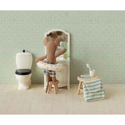 Ein plush brauner mausplüsch in blau gestreiften shorts mit weißem, gelb gepunktetem schwimmring vor mini schminkspiegel nachhaltig ökologische babykleidung schweiz