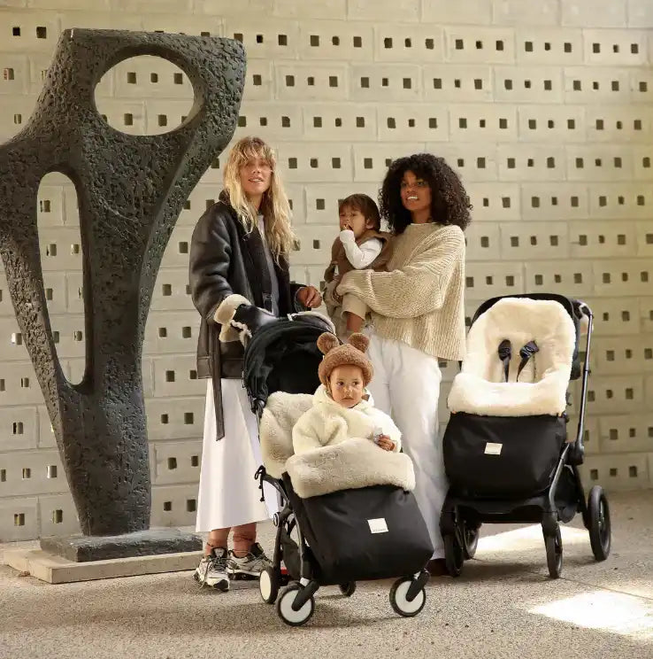 Zwei Frauen mit Babys und zwei Kinderwagen, einer mit einem Baby darin.